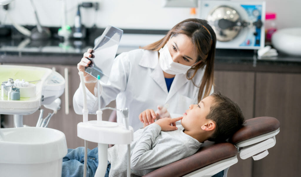 Ethnic Waman dentist holding a x-ray for a kid PEDIATRIC DENTISTS cover for prodent search